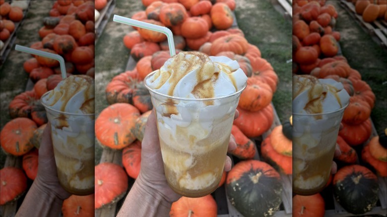 A hand holding an ice cream float with caramel sauce in front of a pile of pumpkins