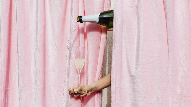 Person trying to pour champagne into a flute behind a pink curtain