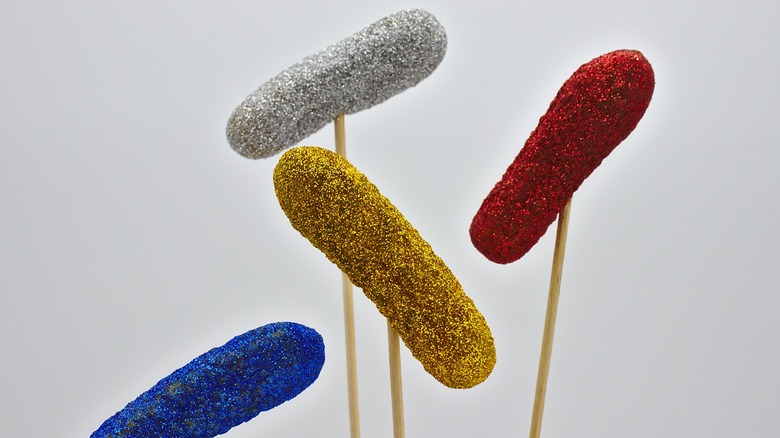 Four pickles dipped in glitter and displayed on sticks.