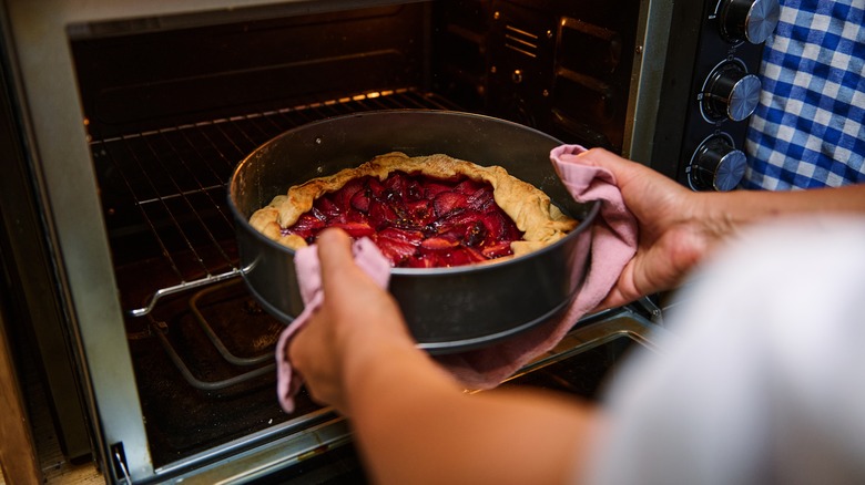 Person holding a pie in a pie tin and taking it out of the oven