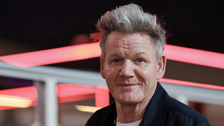 Gordon Ramsay smiling at camera in front of neon lights