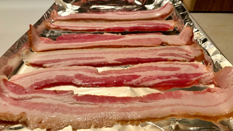 raw bacon strips on foil-lined baking sheet