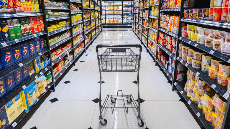 An aisle im a supermarket with an empty cart in the middle of the aisle