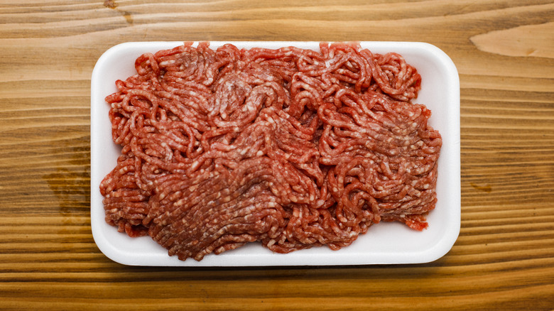 Raw ground beef in styrofoam container on a wooden table