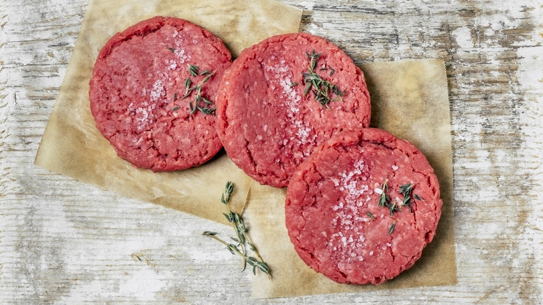 Raw ground beef burgers on paper with rosemary