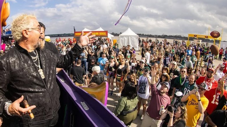 Guy Fieri at Guy's Flavortown Tailgate Party, surrounded be security and fans on Mardi Gras float