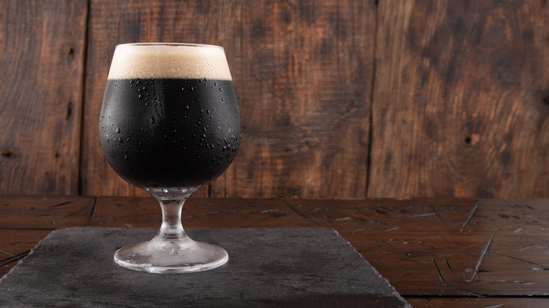 Glass of dark beer, sweating in its glass, on a wooden background