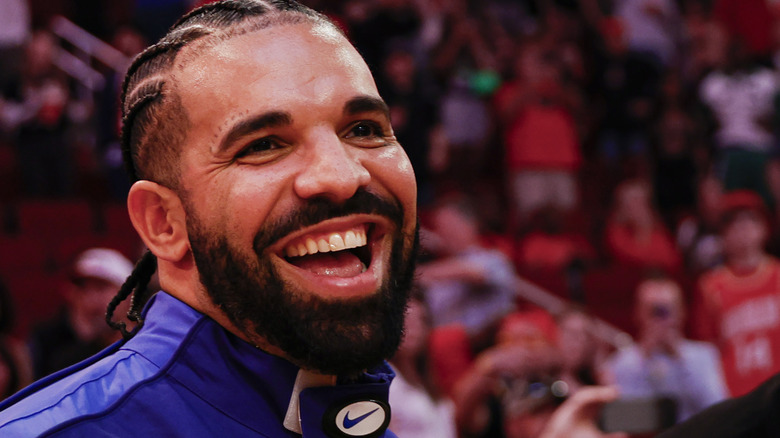 Drake smiles in a sporting event arena