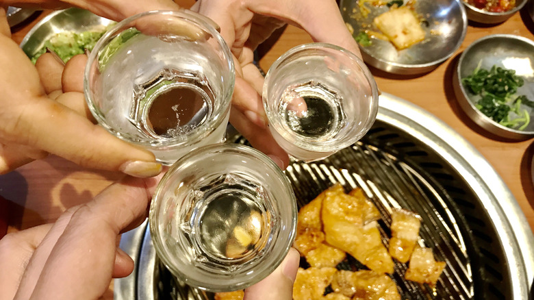 People's hands holding three glasses of soju at a table with Korean barbecue food