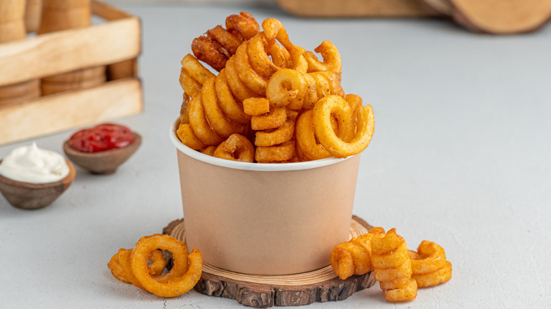 Curly fries in a paper cup with mayo and ketchup