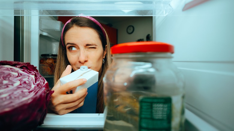 woman sniffing milk carton from fridge