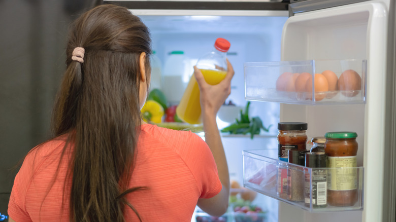 A woman grabbing a container of juice from the refrigerator