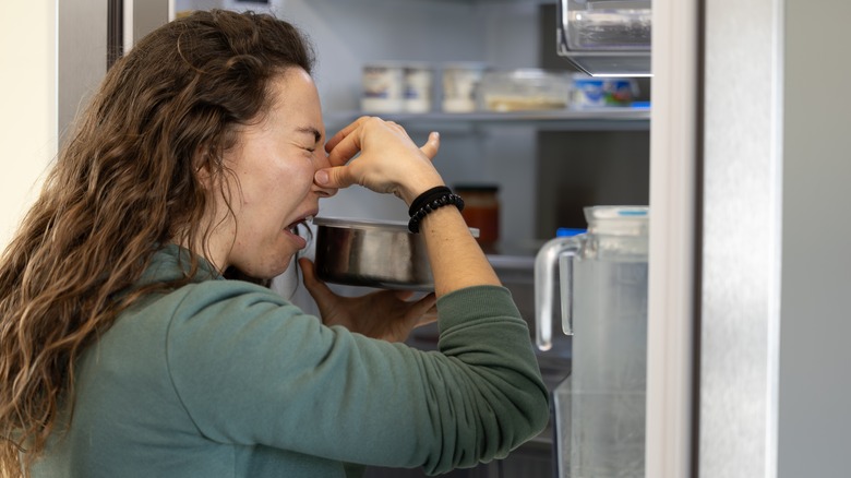 a woman standing in front of a fridge, holding her nose