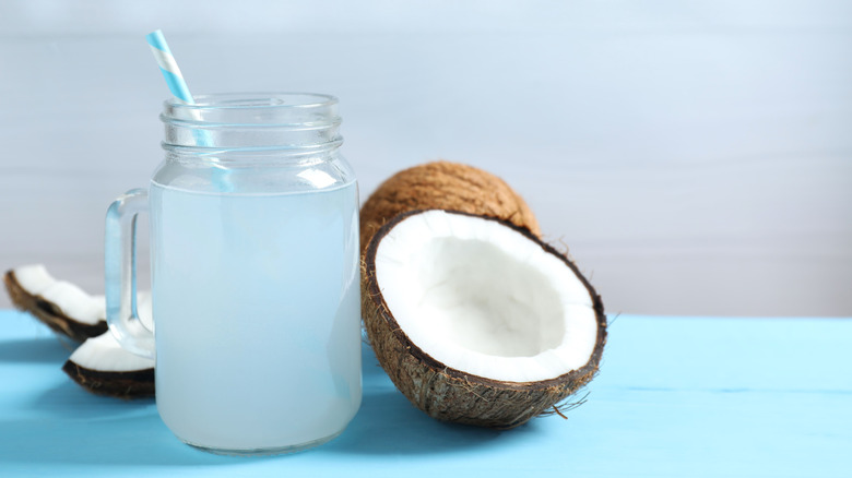 coconut water in a glass mason jar with a handle and coconuts around it