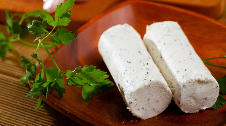 Two logs of goat cheese on wood plate with parsley