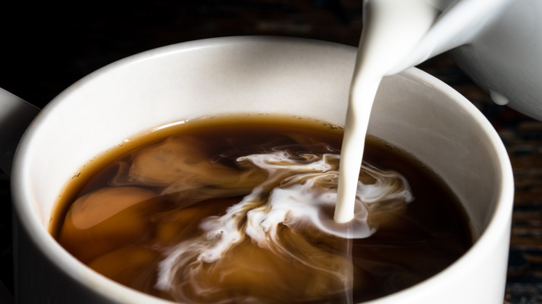 Half and half being poured into a black coffee.