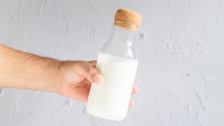 A person holding a glass carafe of milk with a cork stopper