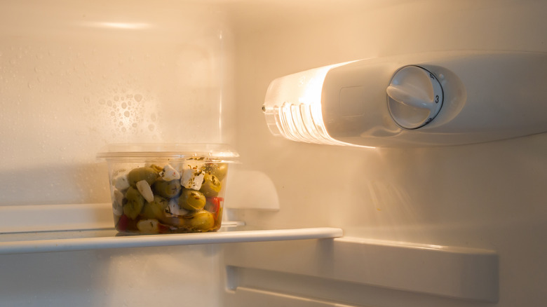 a container of olives and cheese on a fridge shelf