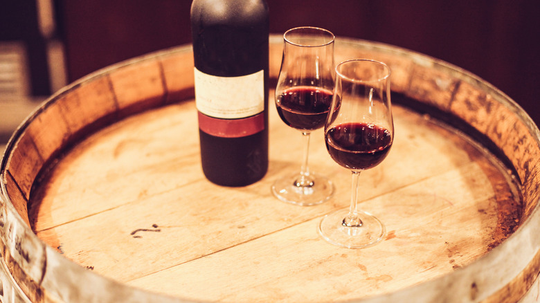 opened port bottle and glasses of port on top of a wooden barrel