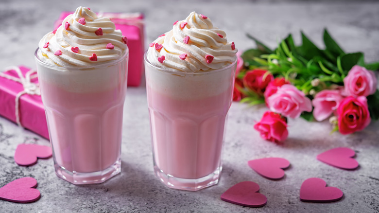 Two pink drinks topped with whipped cream with a bunch of pink roses in the background