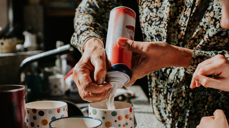 A person spraying whipped cream into coffee mugs