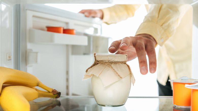 a man reaching for a container of yogurt in fridge