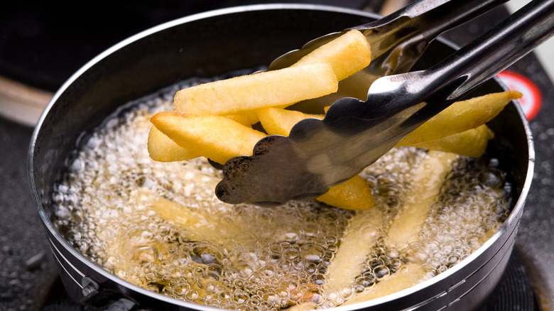 Tongs removing fries from hot oil