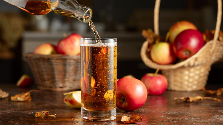 Apple juice being poured into a glass with apples in baskets in the background