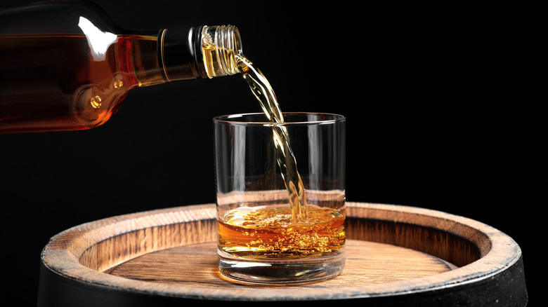 Bourbon being poured into a glass that is on top of a barrel