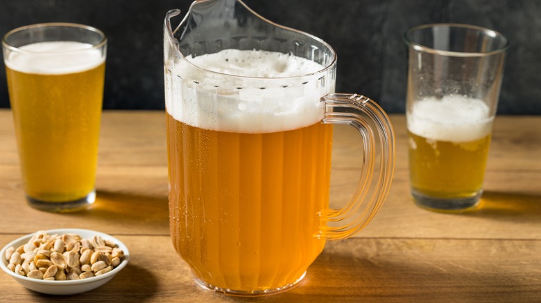 A plastic pitcher of beer with foam on top and pint glasses in the background