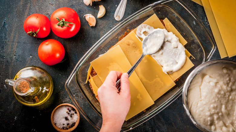 hand spreading bechamel over lasagna noodles with spoon