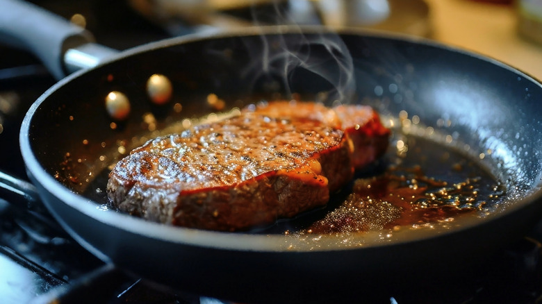 A steak frying in a pan on the stove