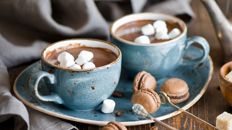 Two blue mugs of hot chocolate on a blue plate with small chocolate macarons