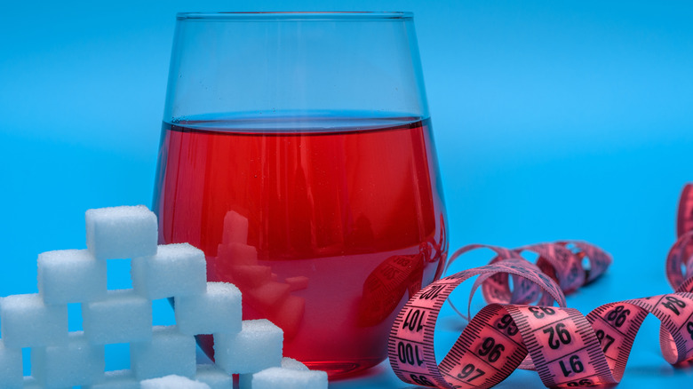 A glass of red wine beside sugar cubes and a measuring tape