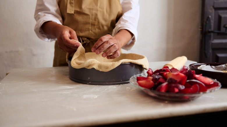 A baker putting a raw pie crust into a pie dish, with berries off to the side.