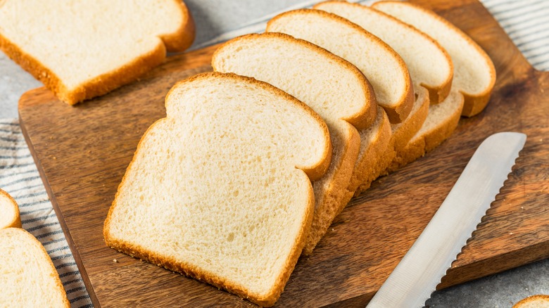 Slices of white bread on a cutting board beside a bread knife