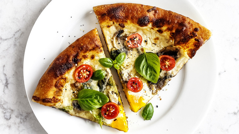 two slices of pizza topped with mushrooms, cherry tomatoes, and basil on a white plate