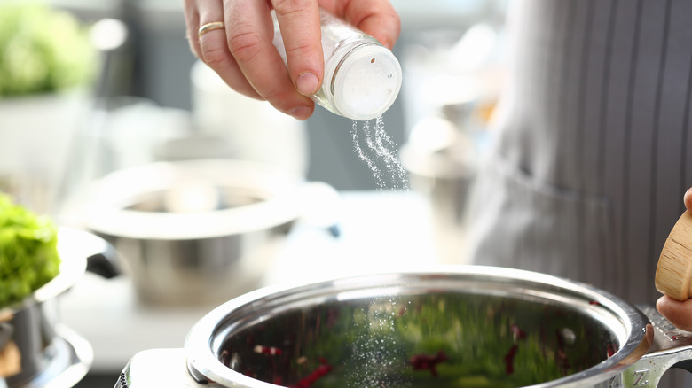 a hand shaking salt into a pot on a stove