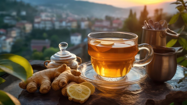 A cup of green tea with ginger root and a lemon slice off to the side