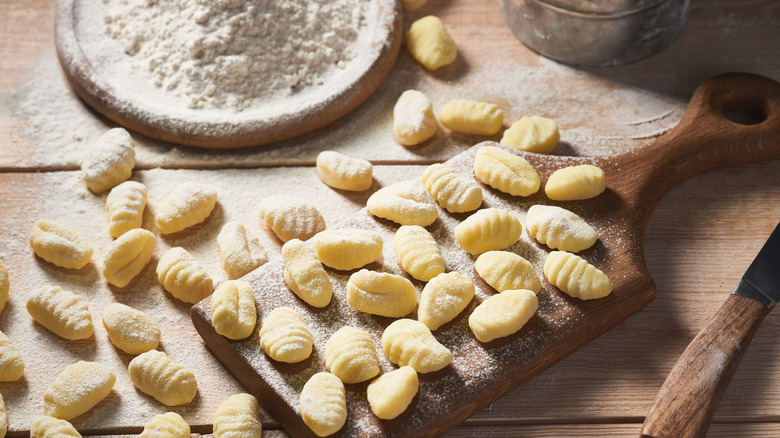 Raw potato gnocchi on a wooden table with a bowl of flour