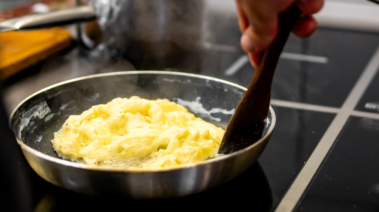 A person stirring a pan of scrmabled eggs on the stove