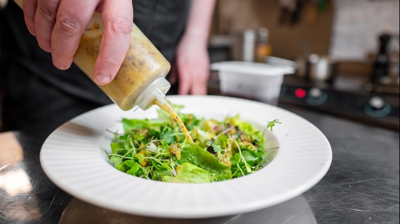 Chef drizzling squeeze bottle of dressing over bowl of salad