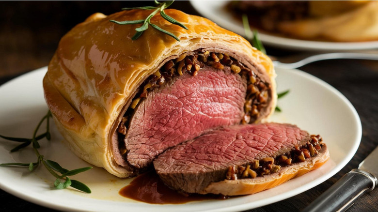 A beef Wellington on a white plate, with one piece sliced off