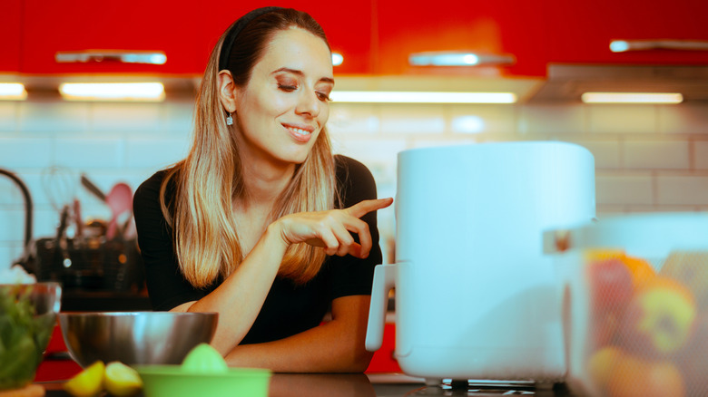 A woman adjusts settings on a white air fryer in a brightly-colored kitchen