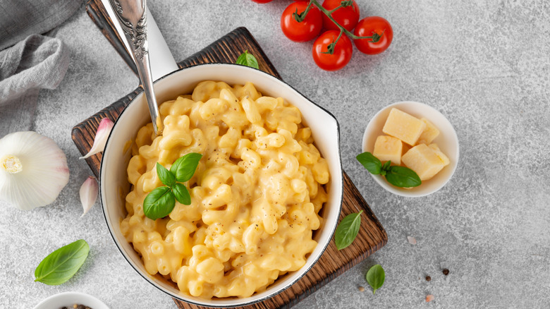 A top view of a bowl of creamy mac and cheese next to butter and tomatoes