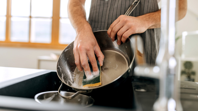 Man washing a pot with dish soap and a sponge