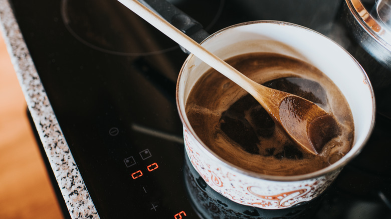 A saucepan filled with gravy cooking on an electric range, with a wooden spoon in it