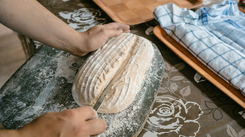 Scoring bread dough lengthwise with bread lame