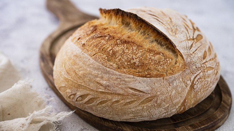 A baked and scored sourdough loaf on a wooden board.