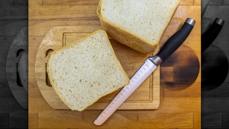 Serrated knife with white bread on a wooden cutting board.